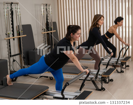 Three Asian women doing Pilates on a reformer. Three Asian women doing Pilates on a reformer. 131337234