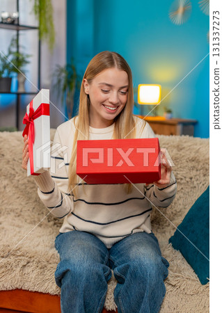 Caucasian woman opening birthday surprise gift on sofa smiling excited indoors happy joyful reaction 131337273