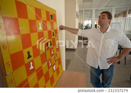 Caucasian man standing at wall mounted magnetic chessboard demonstration.  131337274