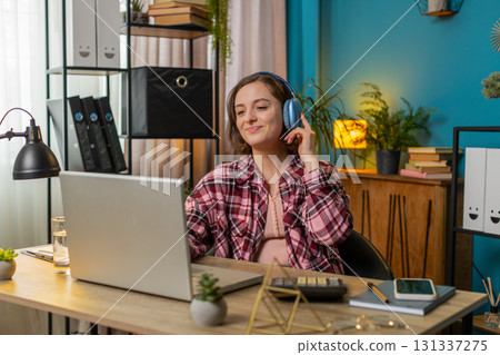 Excited business woman listening music through wireless headphones sitting at home office table 131337275