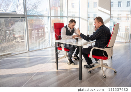 Two Caucasian men using smartphones while sitting at a desk.  131337480