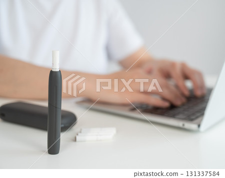 A woman smokes an electronic cigarette while working on a laptop. Tobacco heating system. 131337584