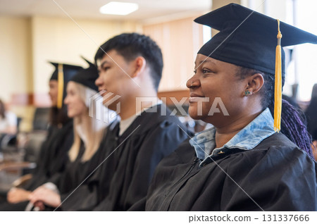 Young people in graduation gowns listen to a speech by a classmate.  131337666