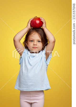 cute little child girl holding a pomegranate on yellow background. cute little child girl holding a pomegranate on yellow background. 131337848