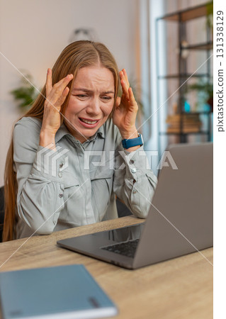 Upset displeased woman freelancer using laptop reading bad news sitting at table in living room Upset displeased woman freelancer using laptop reading bad news sitting at table in living room 131338129