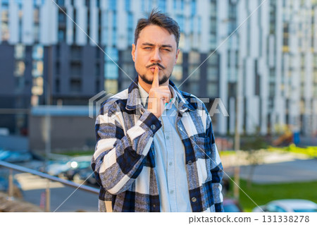 Caucasian man presses index finger to lips makes silence hush gesture sign on downtown city street 131338278
