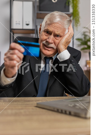 Caucasian angry senior businessman trying to pay online with smartphone blocked credit card at home Caucasian angry senior businessman trying to pay online with smartphone blocked credit card at home 131338330