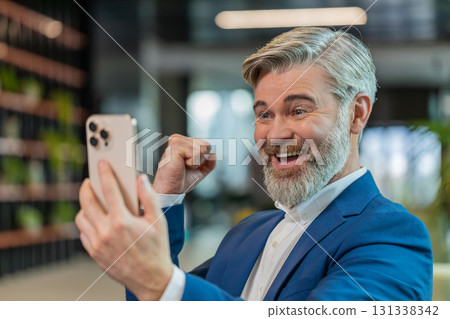 Amazed businessman using smartphone shocked by sudden victory lottery win in modern office lobby 131338342