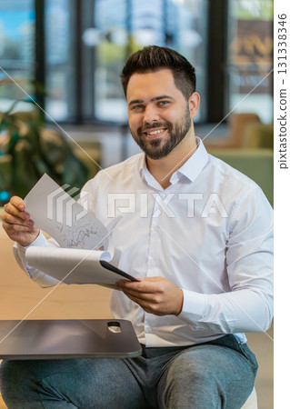 Happy Caucasian young male entrepreneur in formal analyzing graph documents reports in office lobby Happy Caucasian young male entrepreneur in formal analyzing graph documents reports in office lobby 131338346