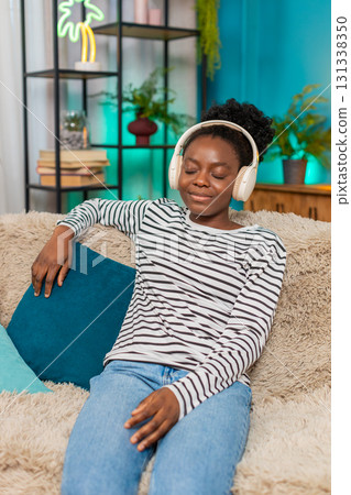 African American woman relaxing sofa eyes closed deep breaths listening music headphones indoors 131338350