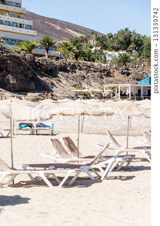 Beach beds and umbrellas lined up on the sandy beach under the blue sky and bright sunlight on Fuerteventura Beach beds and umbrellas lined up on the sandy beach under the blue sky and bright sunlight on Fuerteventura 131339742