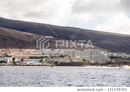 White sandy beaches, resort hotels, and brown bald mountains along the coast seen from the sea on Fuerteventura Island White sandy beaches, resort hotels, and brown bald mountains along the coast seen from the sea on Fuerteventura Island 131339763