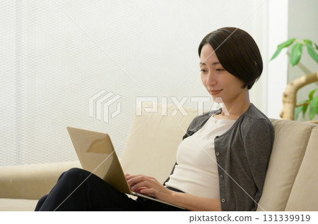 A woman sitting on a couch and operating a computer 131339919