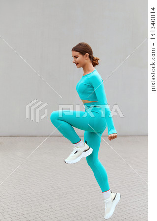 Fitness. Jumping Woman Doing Workout At Outdoor Stadium. Side View Of Fit Girl In Fashion Sporty Outfit Doing Exercise Against Concrete Wall. Dynamic Movement. Fitness. Jumping Woman Doing Workout At Outdoor Stadium. Side View Of Fit Girl In Fashion Sporty Outfit Doing Exercise Against Concrete Wall. Dynamic Movement. 131340014