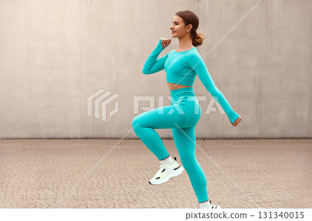 Fitness. Jumping Woman Doing Workout At Outdoor Stadium. Side View Of Fit Girl In Fashion Sporty Outfit Doing Exercise Against Concrete Wall. Dynamic Movement. 131340015