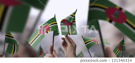 Dominica flags in their hands on a blurred urban background 131340314