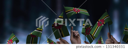 Dominica flags in their hands on a blurred urban background Dominica flags in their hands on a blurred urban background 131340331