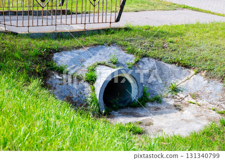 A large concrete pipe is resting on the grass right next to a sidewalk 131340799