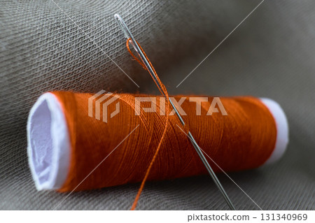 Close up of orange thread and sewing needle Close up of orange thread and sewing needle 131340969