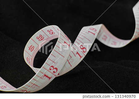 Flexible measuring tape lying on a dark surface Flexible measuring tape lying on a dark surface 131340970