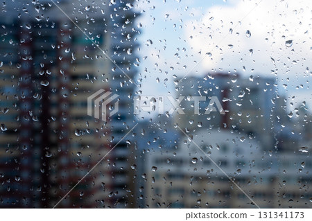 Raindrops gently falling on a window with buildings in the background Raindrops gently falling on a window with buildings in the background 131341173