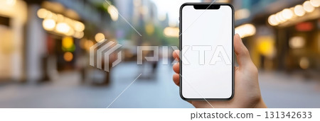 Hand holding a smartphone with a blank white screen for text or app design, set against a blurred shopping mall background, ideal for showcasing mobile experiences 131342633