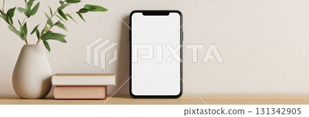 Modern smartphone with blank white screen standing on wooden desk next to books and plant in a vase, perfect for showcasing mobile app or website design 131342905