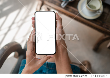 Hands holding a smartphone with a blank screen in a cafe, perfect for app or design mockups. 131343016