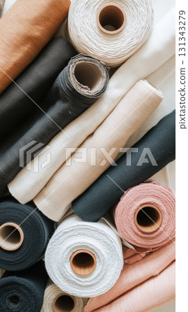 Various rolls of colorful cotton and linen fabrics and sewing threads are neatly arranged on a table, showcasing a collection of materials ready for dressmaking and tailoring Various rolls of colorful cotton and linen fabrics and sewing threads are neatly arranged on a table, showcasing a collection of materials ready for dressmaking and tailoring 131343279