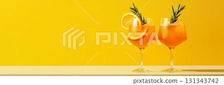 Two glasses of refreshing cocktails, garnished with orange slices and rosemary sprigs, resting on a table against a vibrant yellow backdrop, evoke a cheerful summer vibe 131343742