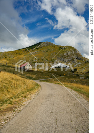 Scenic road winding through golden hills with mountains in the background under a clear blue sky. Ideal for travel, landscape, and nature projects 131344065