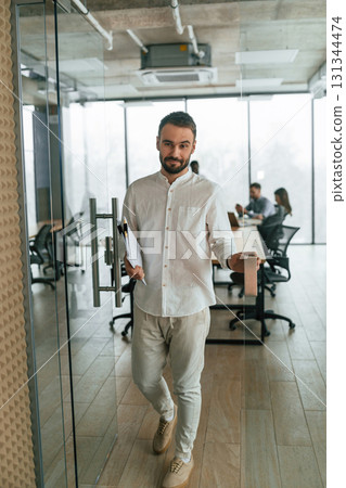 Handsome man with documents. Team of office workers are together indoors Handsome man with documents. Team of office workers are together indoors 131344474