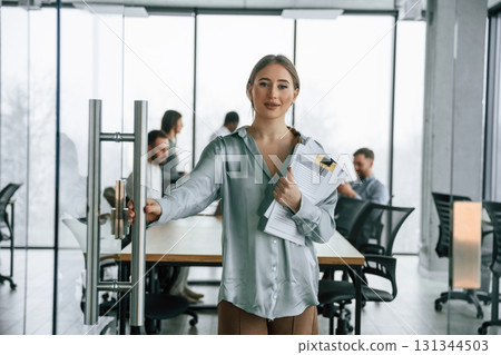 In formal clothes. Woman is standing with documents. Team of office workers are together indoors In formal clothes. Woman is standing with documents. Team of office workers are together indoors 131344503
