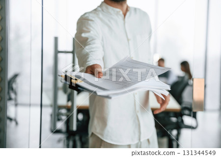 Guy is giving the documents. Team of office workers are together indoors 131344549