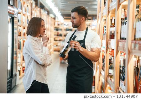 Customer service. The shop owner helps a young woman to choose a good wine 131344907