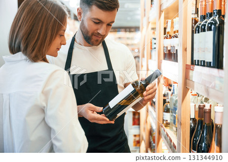 Asking for help. The shop owner helps a young woman to choose a good wine 131344910