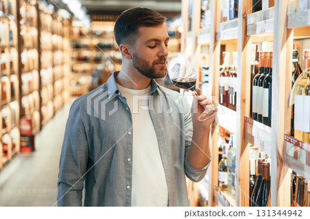 Looking at glass with drink. Man is choosing wine in the store 131344942