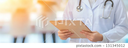 Close up of a female doctor wearing a stethoscope and holding a clipboard, standing in a blurred hospital corridor, conveying professionalism and medical expertise 131345012