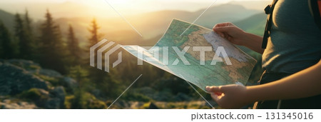 Female hiker is checking her position on a large topographic map during a trekking excursion in a mountain forest at sunset, searching for the right path 131345016