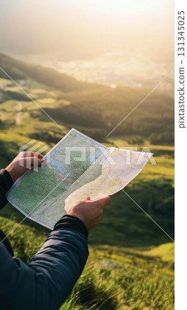 Hands holding a large paper map, revealing a stunning mountain valley bathed in the warm hues of sunset, evoking a sense of adventure and the thrill of exploration 131345025