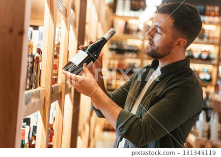 Customer is looking at bottle. Man is choosing wine in the store 131345119