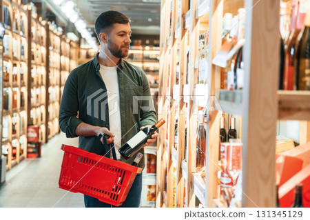 With shopping basket. Man is choosing wine in the store 131345129