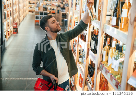 Standing near the shelf. Man is choosing wine in the store 131345136
