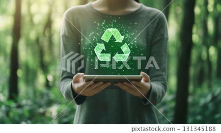 Woman holding tablet displaying a hologram of the recycling symbol promoting sustainability, eco friendly practices, and waste management in environmental conservation 131345188