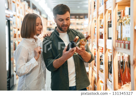Choosing between two different bottles. Man and woman in the wine shop Choosing between two different bottles. Man and woman in the wine shop 131345327