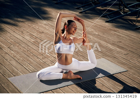 On the yoga mat. Young woman in fitness clothes is outdoors 131345419