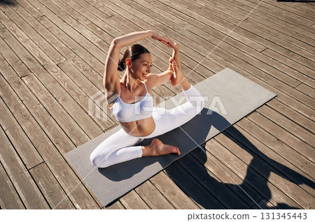 Illuminated by sunlight, practicing yoga. Young woman in fitness clothes is outdoors 131345443