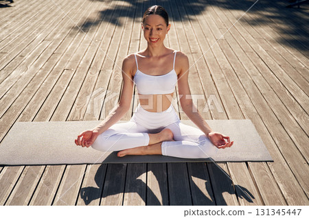 In lotus pose, meditating. Young woman in fitness clothes is outdoors In lotus pose, meditating. Young woman in fitness clothes is outdoors 131345447