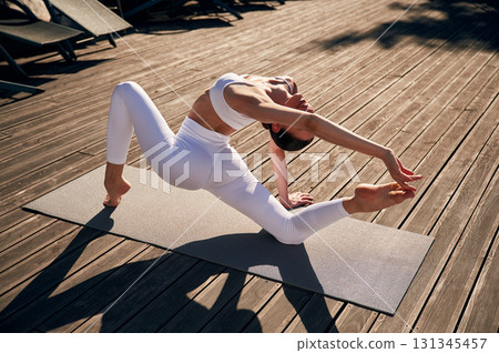 Exercises for flexibility. Young woman in fitness clothes is outdoors Exercises for flexibility. Young woman in fitness clothes is outdoors 131345457