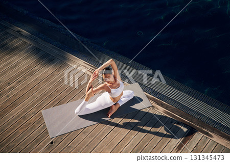 View from the top, doing exercises. Young woman in fitness clothes is outdoors View from the top, doing exercises. Young woman in fitness clothes is outdoors 131345473